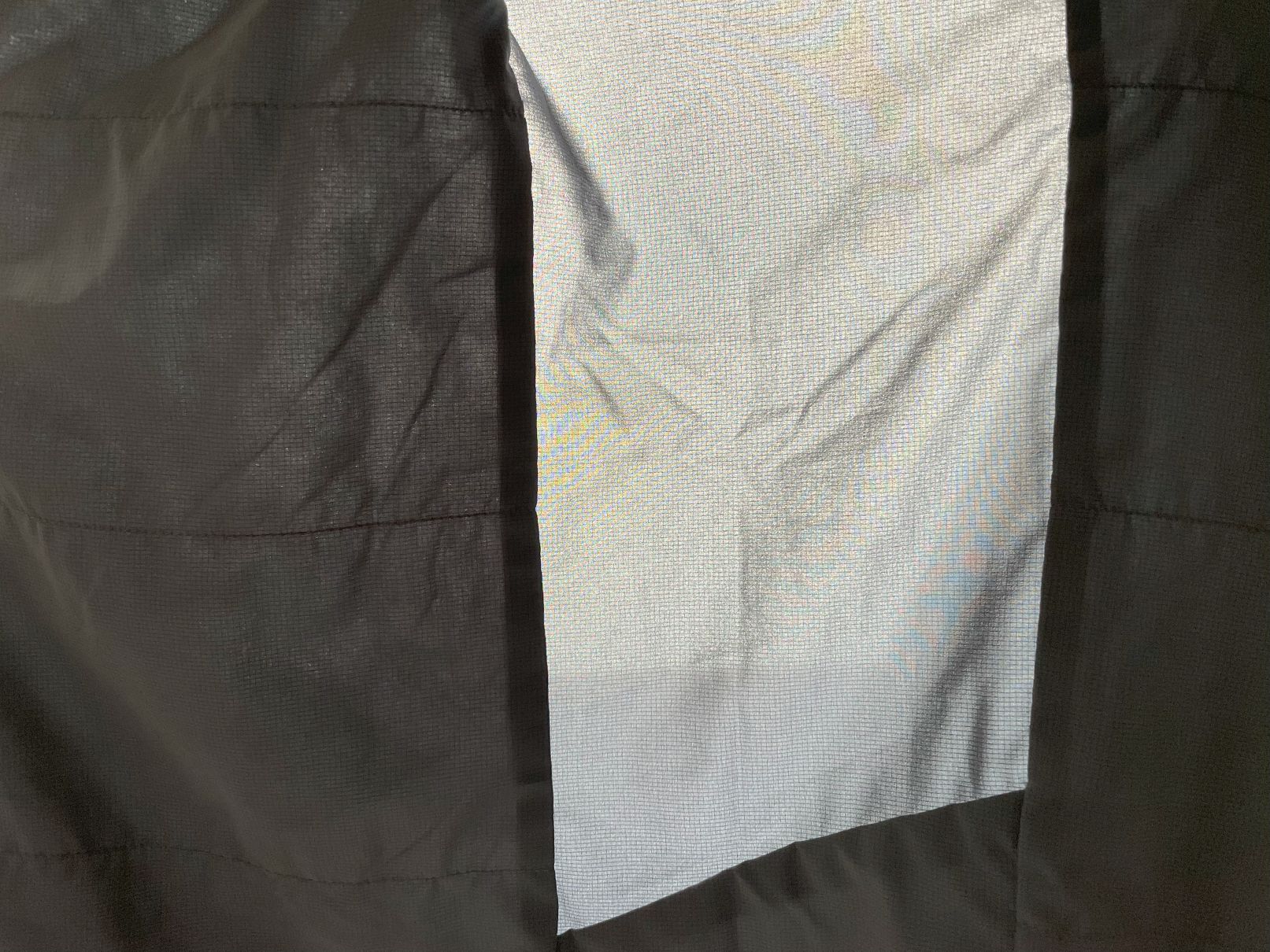 Holding the Patagonia Nano Air Ultralight jacket up to a lamp to see the single layer of fabric under the arms.