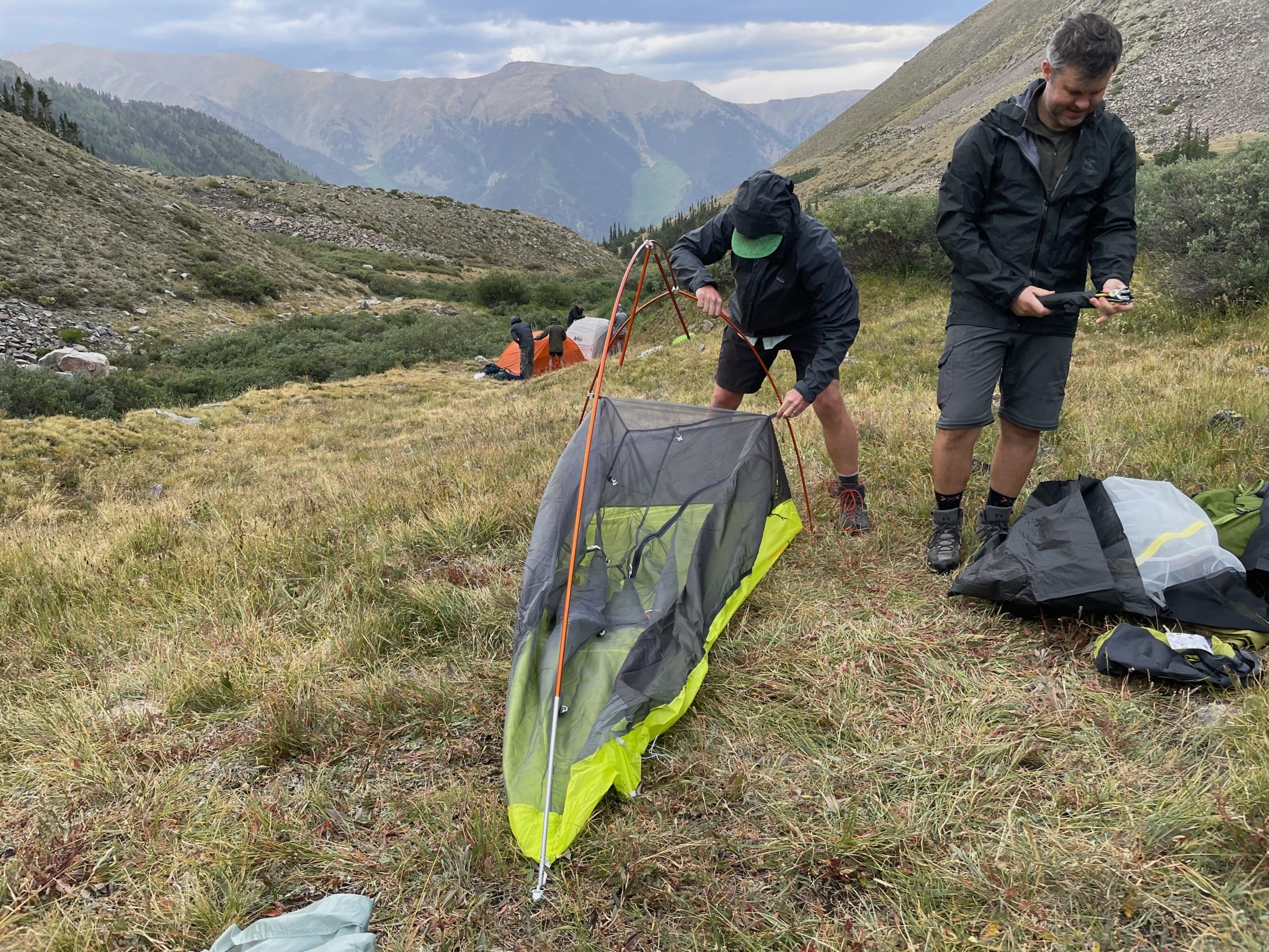 A backpacking pitching the Big Agnes Tiger Wall 1-person tent on a mountain in a light rain.