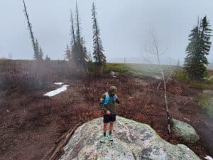 A trail runner standing on a rock in the rain wearing the Arc'teryx Norvan Jacket.
