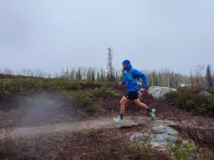 Trail running in the rain wearing the men's Patagonia Storm Racer jacket in blue.