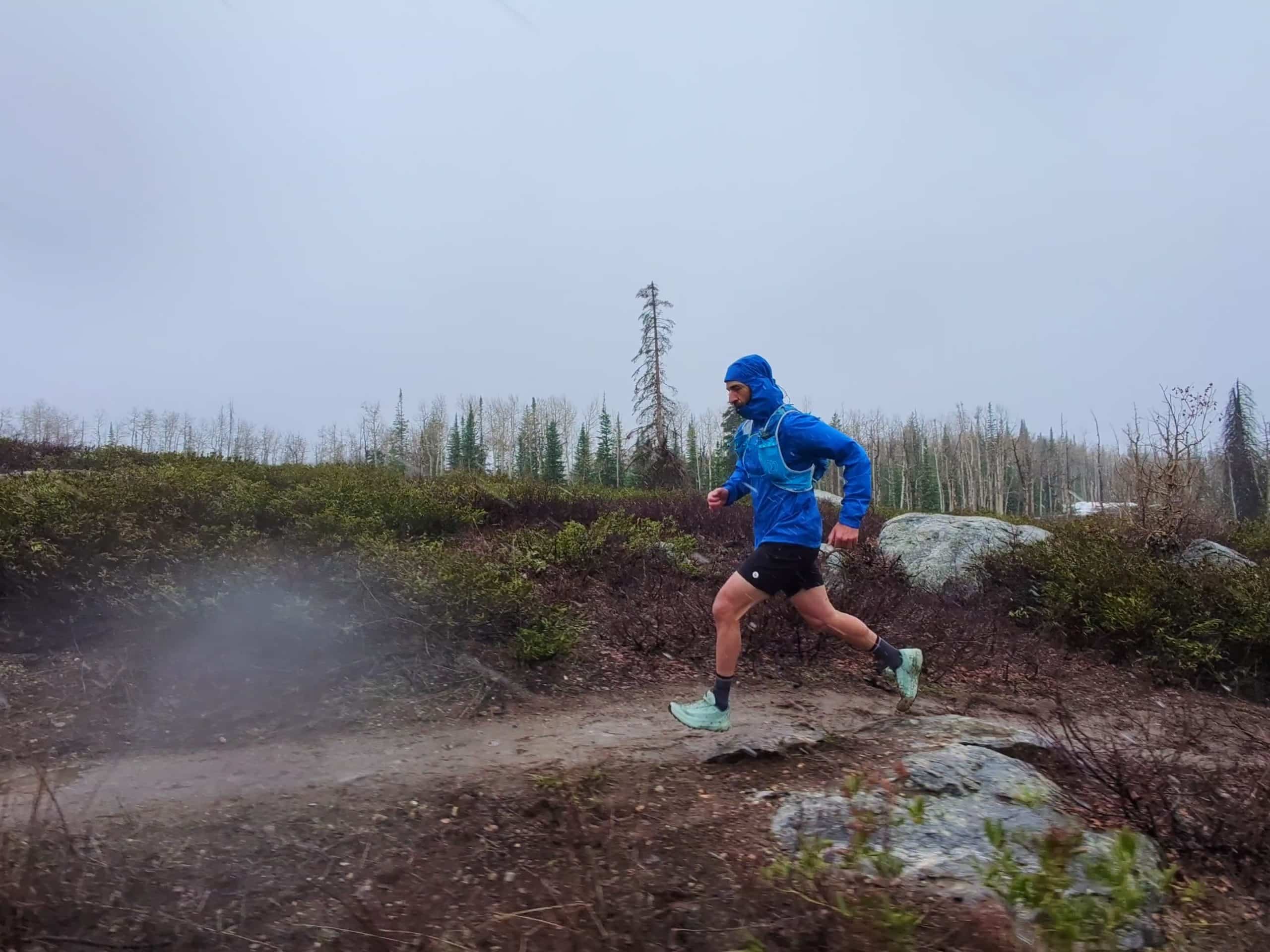 Trail running in the rain wearing the men's Patagonia Storm Racer jacket in blue.